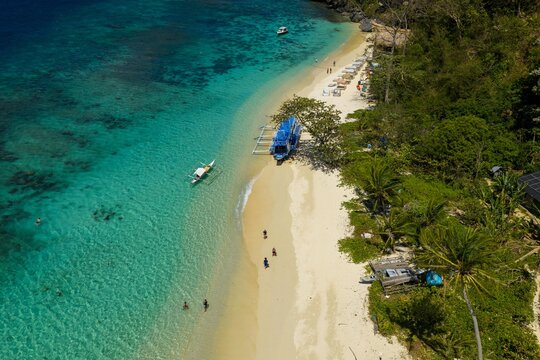Aerial view of Seven Commando Beach, El Nido, Palawan. Turquoise waters, white sand beach, and palm trees in a tropical paradise, Palawan, Philippines.