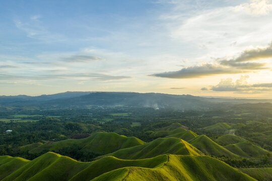Aerial sunrise over Alicia Panoramic Park, Bohol. Rolling green ridges of Binabaje Hills under golden light, scenic tropical mountain landscape in the Philippines.