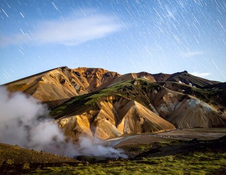 Landmannalaugar rhyolite mountains at night with geothermal steam. Sharp multicolored ridges, natural hot spring, and starry sky with deep focus and copy space. Iceland nature concept.