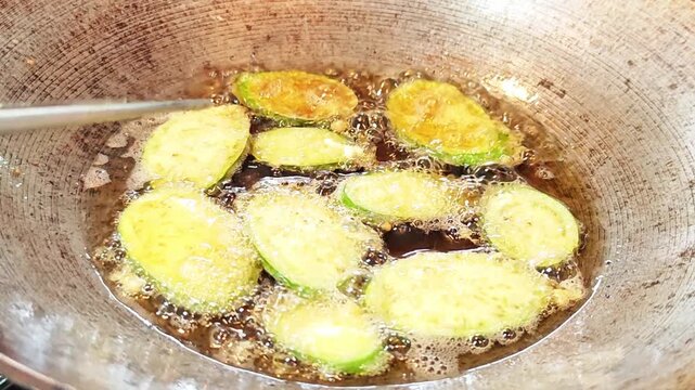Preparing golden fried egg-coated eggplant slices in a metal wok, cooking process.