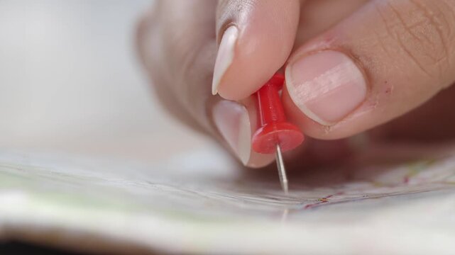 Close up view of hand placing red push pin on paper map for travel planning and destination tracking