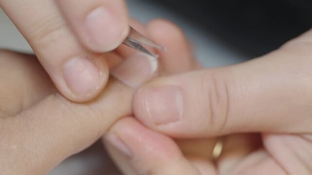A close up view of a manicurist carefully trimming excess cuticle skin around fingernails using specialized nail clippers during a professional manicure session