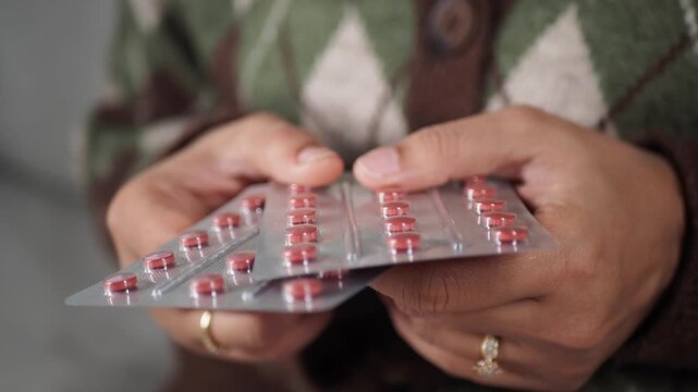 Woman's hands holding two blister packs of red pills, demonstrating medicine packaging and pharmaceutical products