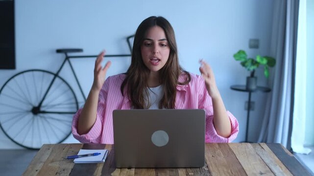 A young woman experiences frustration and exhaustion while working on her laptop from home. She throws her hands up in exasperation, highlighting the challenges of remote work and potential burnout.