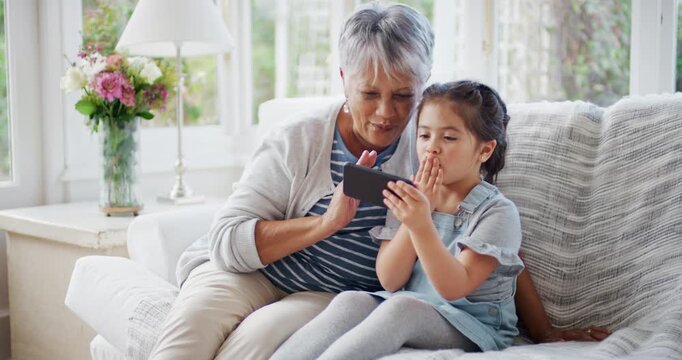 Grandmother, girl and phone on couch with video call, wave goodbye or bonding together on weekend break. Happy, old woman and grandchild in home with tech, contact or blow kiss for virtual connection