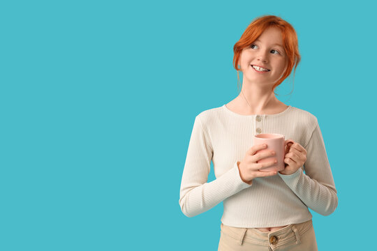 Teenage redhead girl with cup of sweet cocoa on blue background