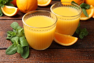 Citrus juice in glasses, fresh oranges and mint leaves on wooden table, closeup © New Africa