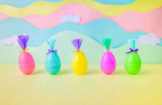 Bright plastic easter eggs wrapped as gifts on pastel rainbow background with clouds festive spring decoration minimal composition.