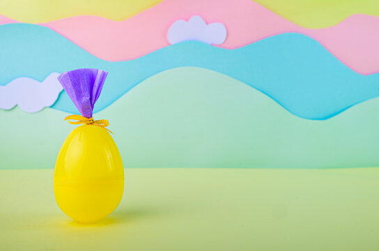 Bright yellow easter egg wrapped as gift on pastel landscape background with clouds festive spring decoration concept.