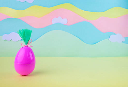 Bright pink easter egg wrapped as gift on pastel landscape background with clouds festive spring decoration concept.