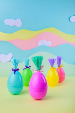 Bright plastic easter eggs wrapped as gifts on pastel rainbow background with clouds festive spring decoration minimal composition.