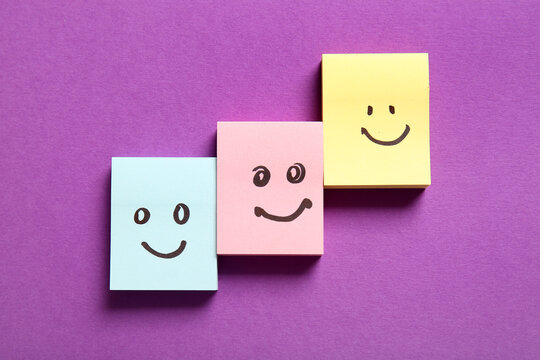 Stacks of sticky papers with drawn happy faces on purple background