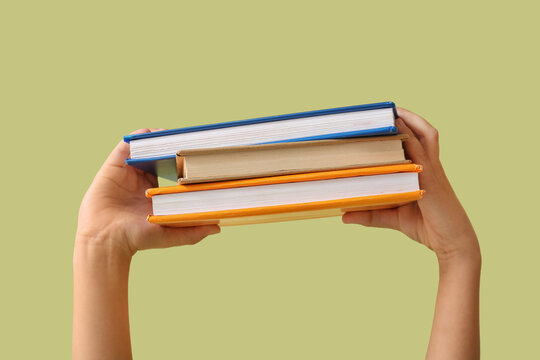 Child's hands with stack of books on green background