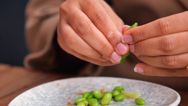 A close up view of a person preparing delicious edamame, shelling the green beans with their hands in a natural light setting