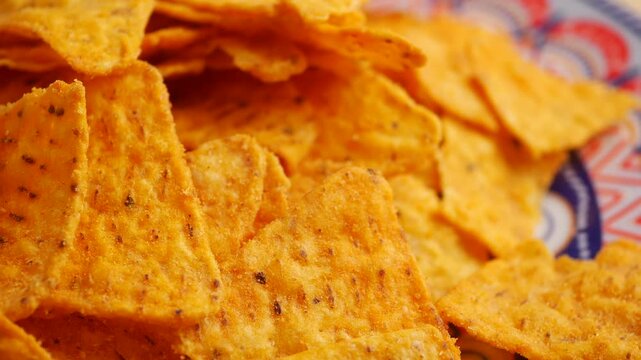 Extreme close up of crunchy corn tortilla chips rotating on blue patterned plate for snack appetizer