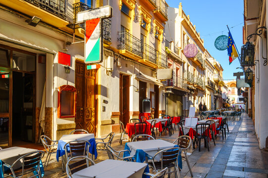 A narrow alley of sidewalk cafes and restaurants in the historic old town center of the Andalusian city of Ronda, Spain.