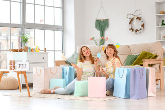 Happy young women with paper shopping bags and decor for Easter at home