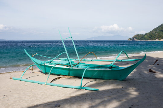 Green traditional outrigger boat on tropical beach
