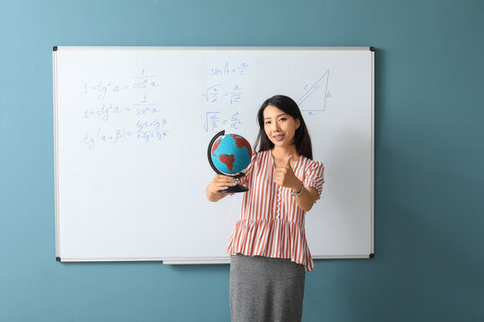 Female Asian teacher with globe near flipboard in classroom