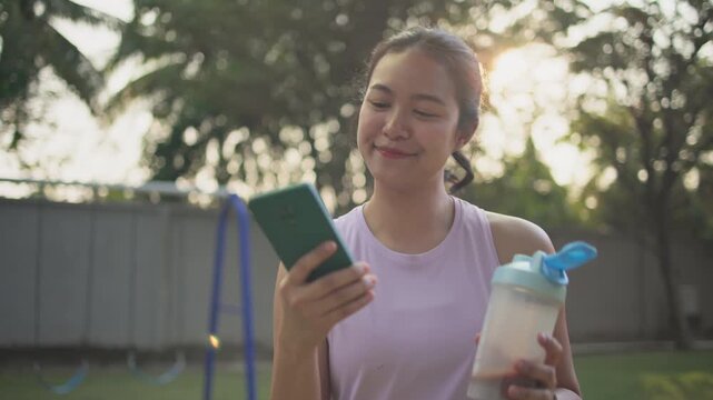 Young active woman drink whey protein shake bottle eating diet food using phone calorie AI plan app after workout health care asia people happy relax anti aging life weight loss public green park walk