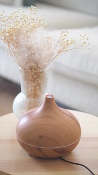 Wood grain electric oil diffuser emitting steam on wooden table with vase of flowers
