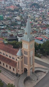 Vertical screen Aerial Perspective Over Da Lat Cathedral And Dense City Backdrop, Tall Spire Framed By Colorful Houses, Contrast Between Sacred Architecture And Everyday Urban Fabric,