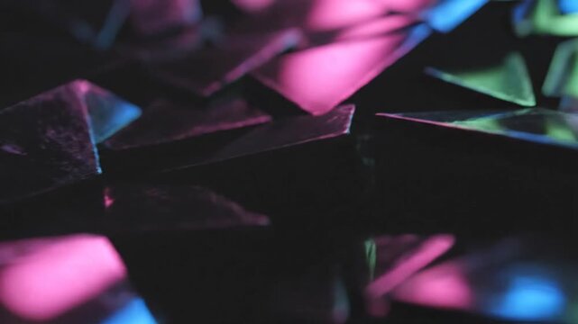 Close-up of dark multi-faceted geometric surfaces reflecting vibrant neon pink, blue, and green light. Abstract sharp edges on metallic shards with a shallow depth of field.