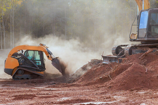 Two construction machines dig move dirt at work site with dust rising in air