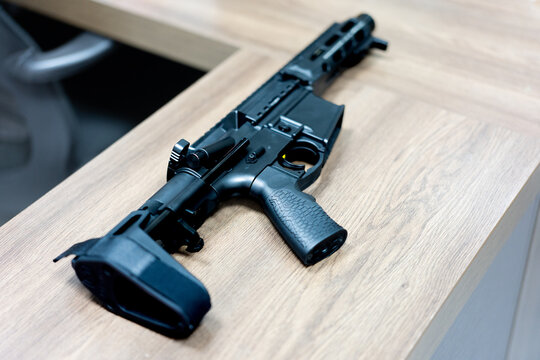 Black tactical rifle with suppressor resting on wooden table in modern indoor setting