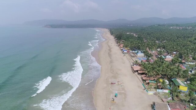 Aerial drone view of Agonda Beach coastline with waves and palm trees in South Goa, India