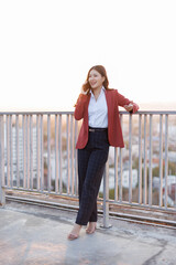 Obraz premium A charming businesswoman dressed in tailored attire enjoying a phone conversation on a rooftop, with a stunning sunset backdrop illuminating her confident and approachable personality.