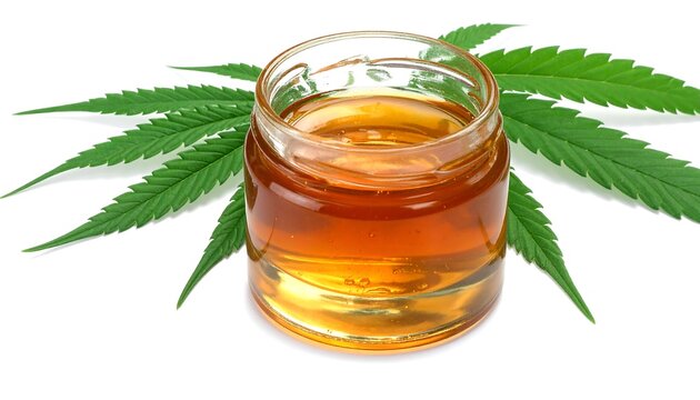 A glass jar of golden liquid with cannabis leaves