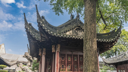 Fototapeta premium Beautiful Chinese pagoda. Roof with curved cornices, ornaments along the edges. Latticed partitions. Green branches of a tree against a blue sky and clouds. China. Shanghai. Yu Garden. Yuyuan