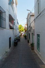Fototapeta premium Bodrum, Turkey. Typical narrow street in the old town featuring whitewashed walls, several parked scooters, and a small blue glimpse of the sea visible through trees at the far end.