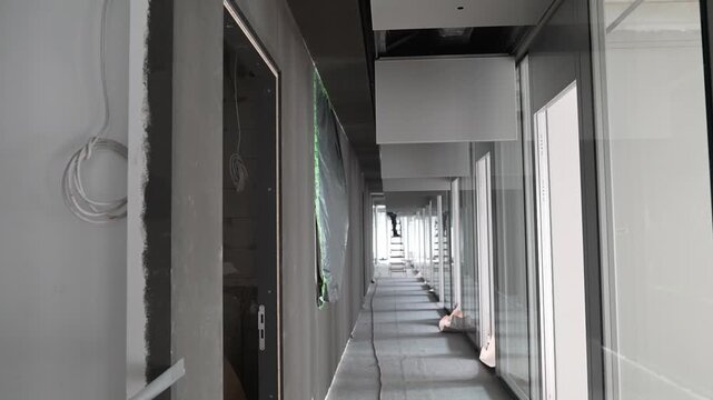 Interior corridor with ceiling panels and glass walls in unfinished building, modern architecture space during fit out phase with suspended ceiling elements and linear perspective