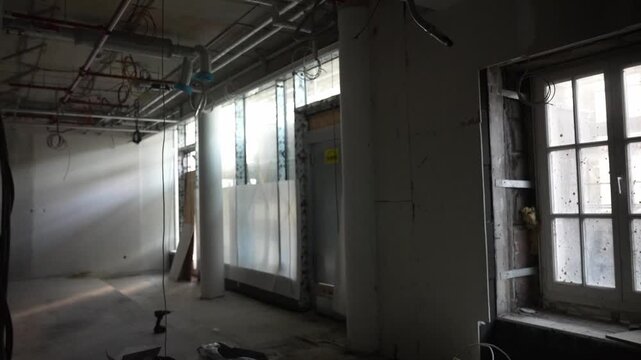 Unfinished building interior with windows, columns and exposed ceiling systems, raw construction space with cables and natural light during renovation phase