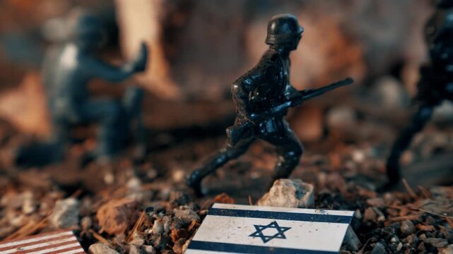 Plastic toy soldiers reenacting a battle scene. Miniatures of an american and an israeli flag lie on the rocky, dirt battlefield