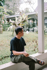 Fototapeta premium Asian Man Sitting and Looking Away Thoughtfully in a Peaceful Garden