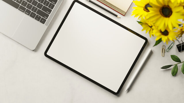Top view white screen tablet and stylus with laptop and book aside sunflower on marble table surface