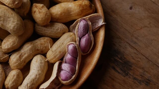Boiled peanuts in shell with purple violet skin kernels revealed on wooden plate on rustic wood table, healthy traditional Asian snack nutrition closeup
