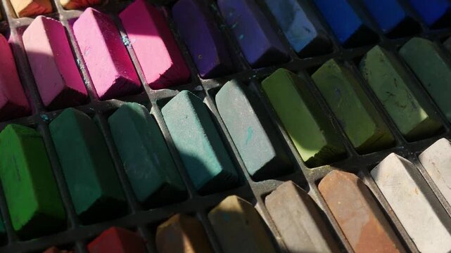 Colorful soft pastel chalk sticks arranged in a worn artist's palette box, vibrant rainbow art supply collection