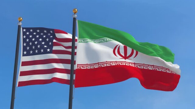 "A symbolic photograph of two national flags flying side by side against a clear blue sky. On the left, the flag of the United States displays thirteen horizontal red and white stripes with a blue can