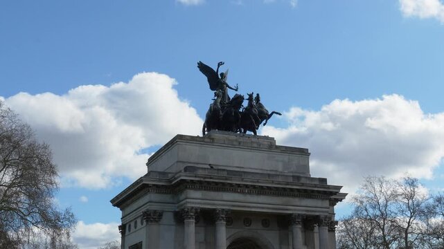 Wellington Arch in London with quadriga statue on top of the arch. Low angle view showing horses and chariot sculpture against blue sky with clouds