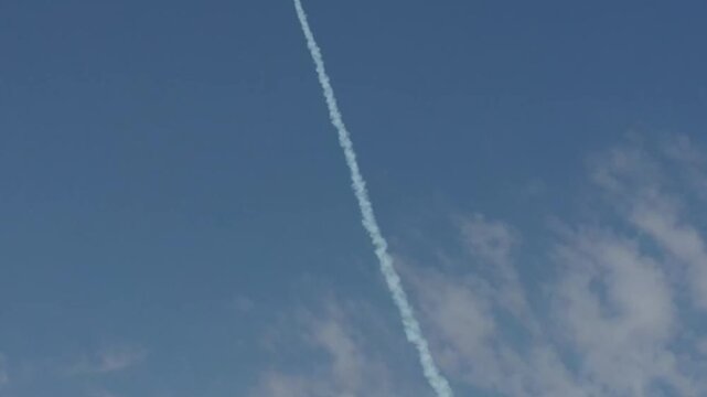 A small rocket launches from a remote desert testing facility into the blue sky leaving a prominent white smoke trail.