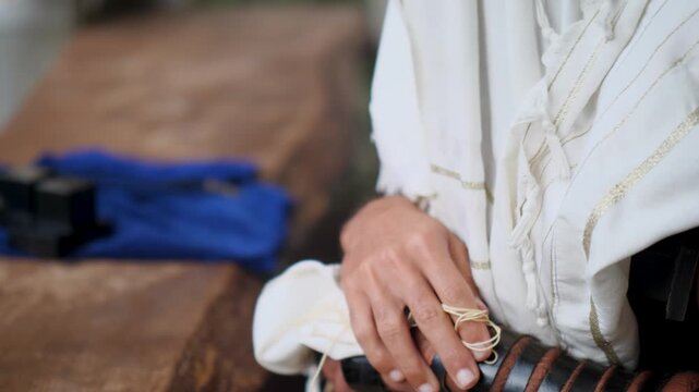 Hands holding tzitzit and prayer book during Jewish prayer ritual.