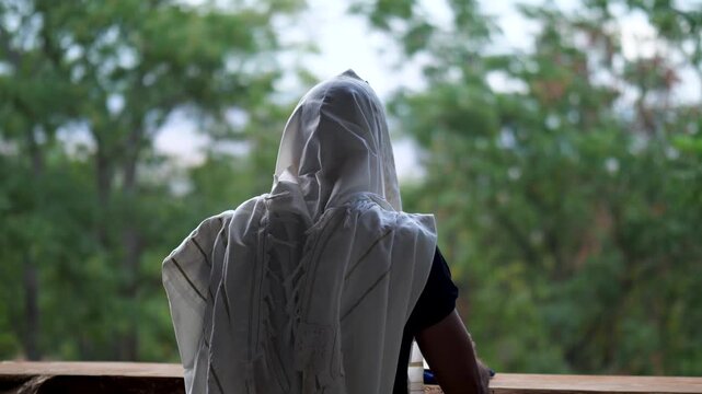 Man praying with tallit, gently swaying while holding prayer book.