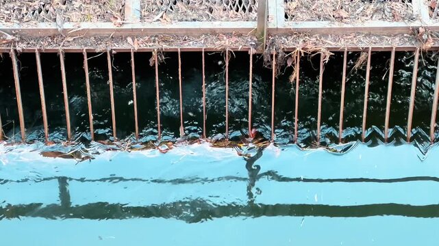 Close-up of a metal grate filtering debris in a canal or drainage system. Ideal for content regarding urban water management, infrastructure maintenance, and flood prevention.