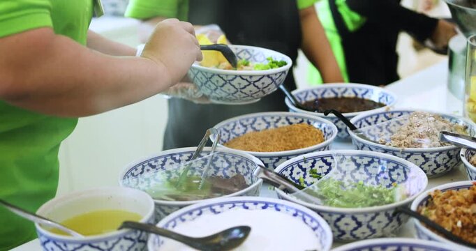 Gloved staff preparing Thai noodle bowl, adding condiments like peanuts, chili and greens, showcasing hygienic street food preparation process