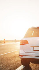 Fototapeta premium Sunset view of a white car parked on a road with orange sky in the background
