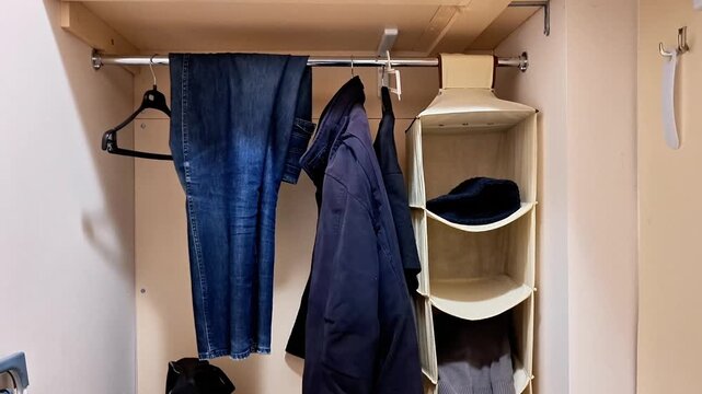 Wardrobe interior with hanging rod holding jeans and a coat, alongside a beige fabric organizer filled with folded clothes, showcasing practical storage and organization